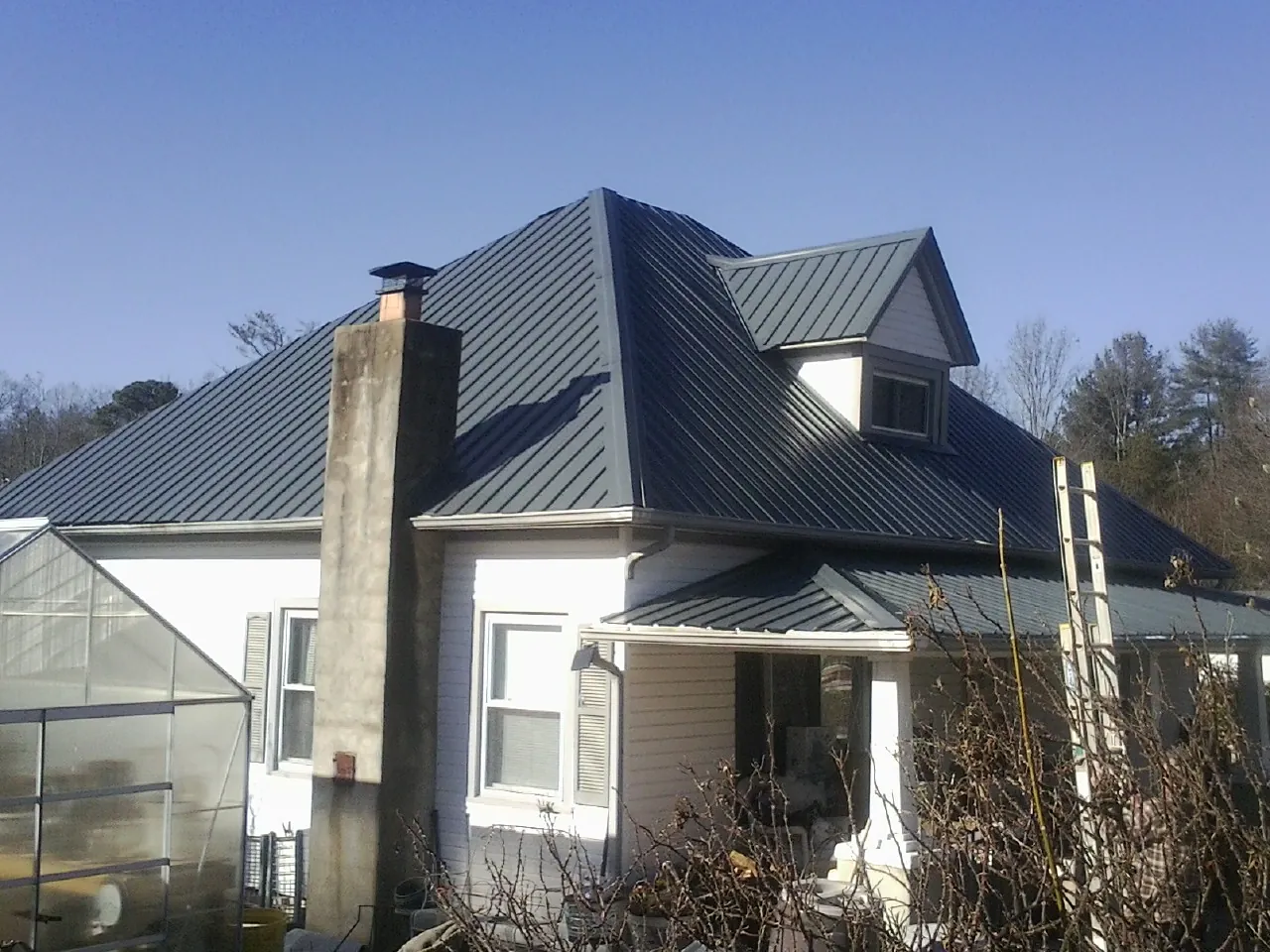Dark blue standing seam metal roof on a white farmhouse with dormer — Slate & Tile Roof Repair by Roofing Brothers in Mill Neck