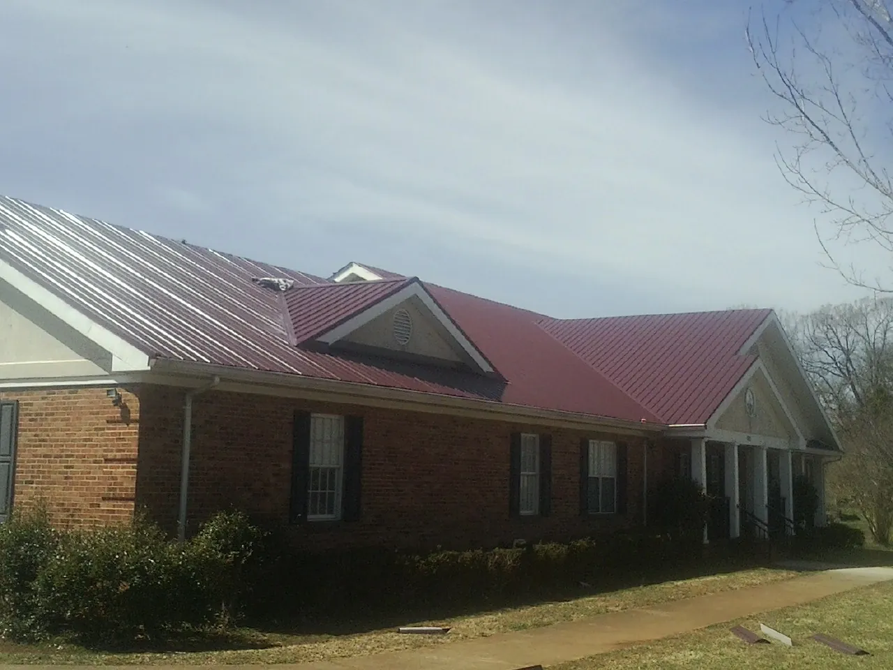Red metal roof with gabled entries on a long brick building, from a Hail Damage Roof Repair job in Mill Neck