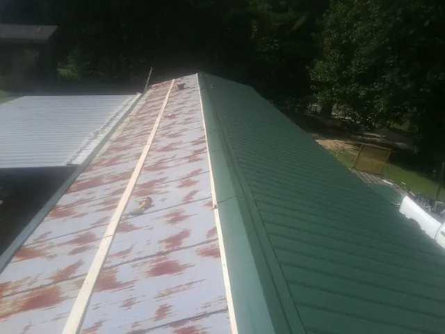 Old rusted panels beside newly installed green metal roofing — Wind Damage Roof Repair by Roofing Brothers in Mill Neck