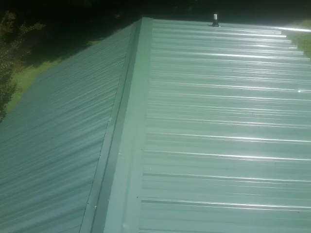 New green metal panels meeting at the ridge of a roof — Flat Roof Repair work by our crew in Mill Neck