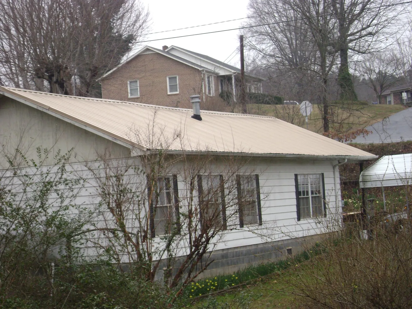 Tan metal roof on a white sided house set into a hillside — Commercial Roofing by Roofing Brothers in Mill Neck
