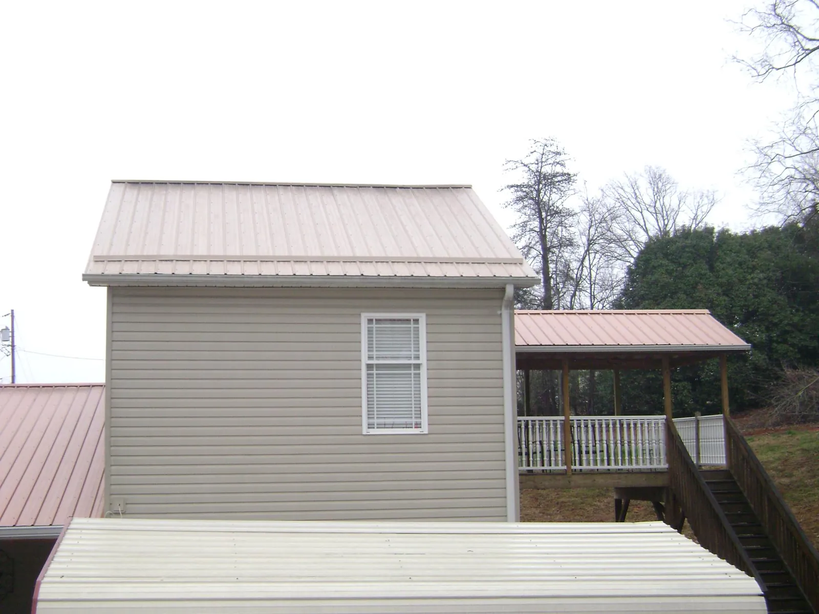 Tan metal roofs on a two story addition and attached porch, from a Roof Replacement job in Mill Neck