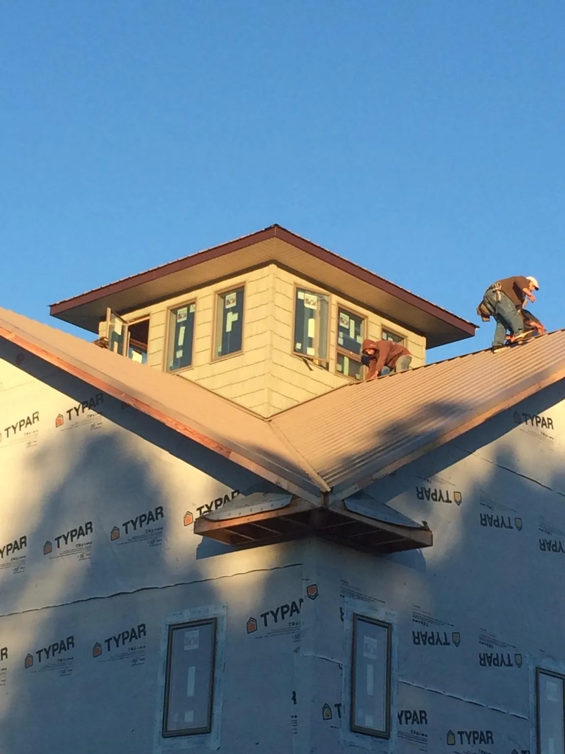 Roofers working around a rooftop cupola on a new metal roof at sunset — Roof Waterproofing in Mill Neck by Roofing Brothers
